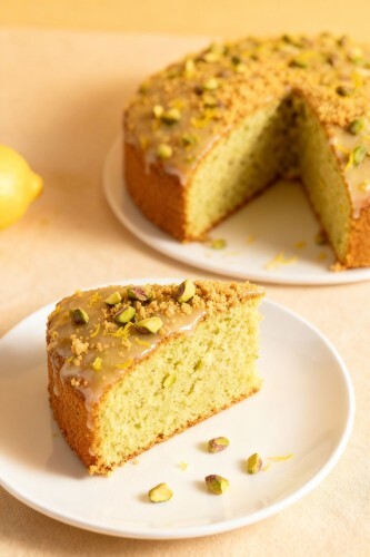 Ein Stück Pistazien-Zitronenkuchen auf einem Teller, bestreut mit gehackten Pistazien und Zitronenzeste.